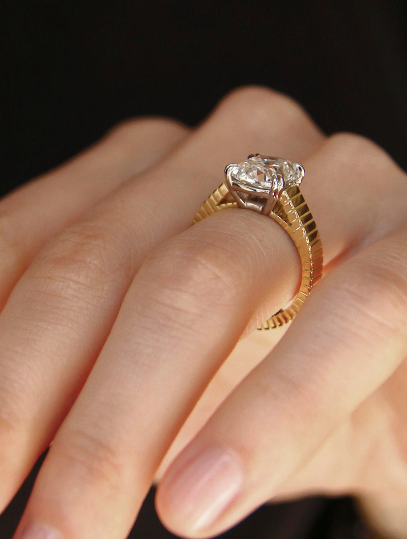 Signature LEIL solitaire 18k yellow gold engagement ring with a ribbed architectural band and a cathedral emerald lab diamond on a hand against a dark background