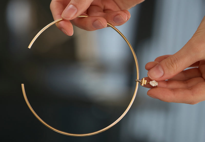 Signature LEIL architectural tubular necklace in 18k yellow gold with a spike lab diamond pendant held by hands against a blurred background