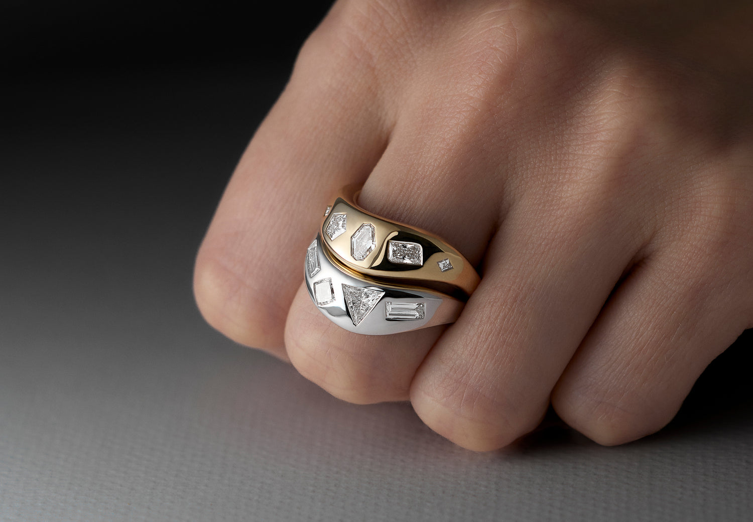 Close-up of a hand wearing two signature LEIL star cluster lab diamond rings in solid 18k yellow and white gold on a dark background