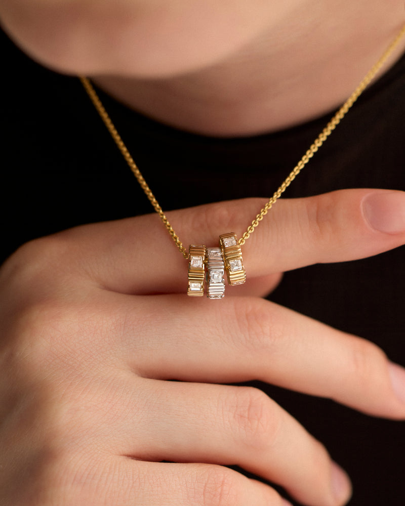 Gold necklace with three LEIL architectural Arra pendants in 9k yellow and white gold with lab diamonds held by a hand against a dark background