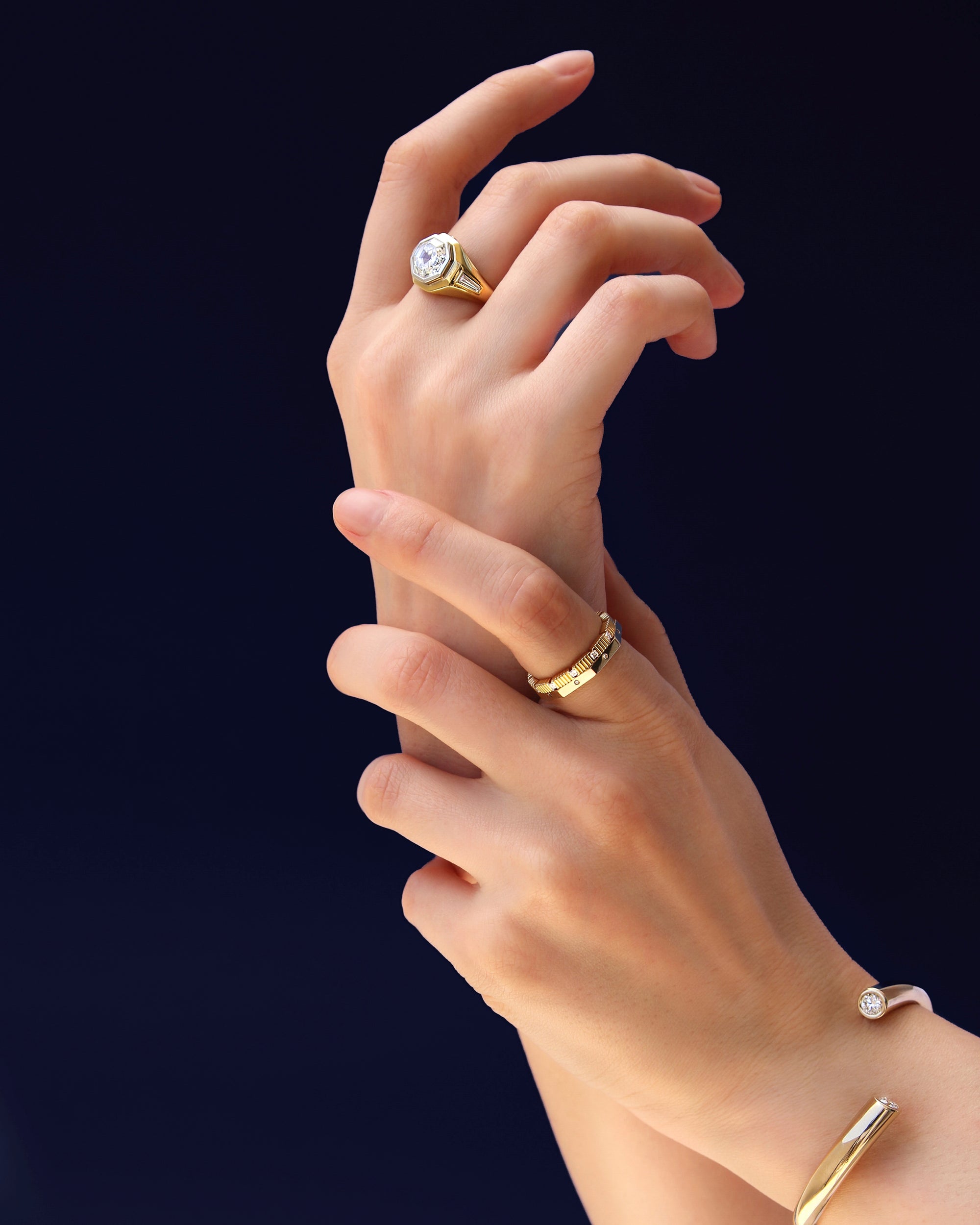 Close-up of hands wearing multiple LEIL fine jewellery pieces including a bracelet and several rings in 18k gold and lab diamonds on a dark background