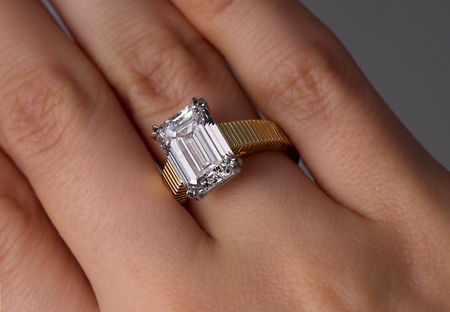 A close-up of a hand wearing a Leil cathedral Arra engagement ring with a large emerald-cut lab-grown diamond with a platinum claw setting and an architectural ribbed band.