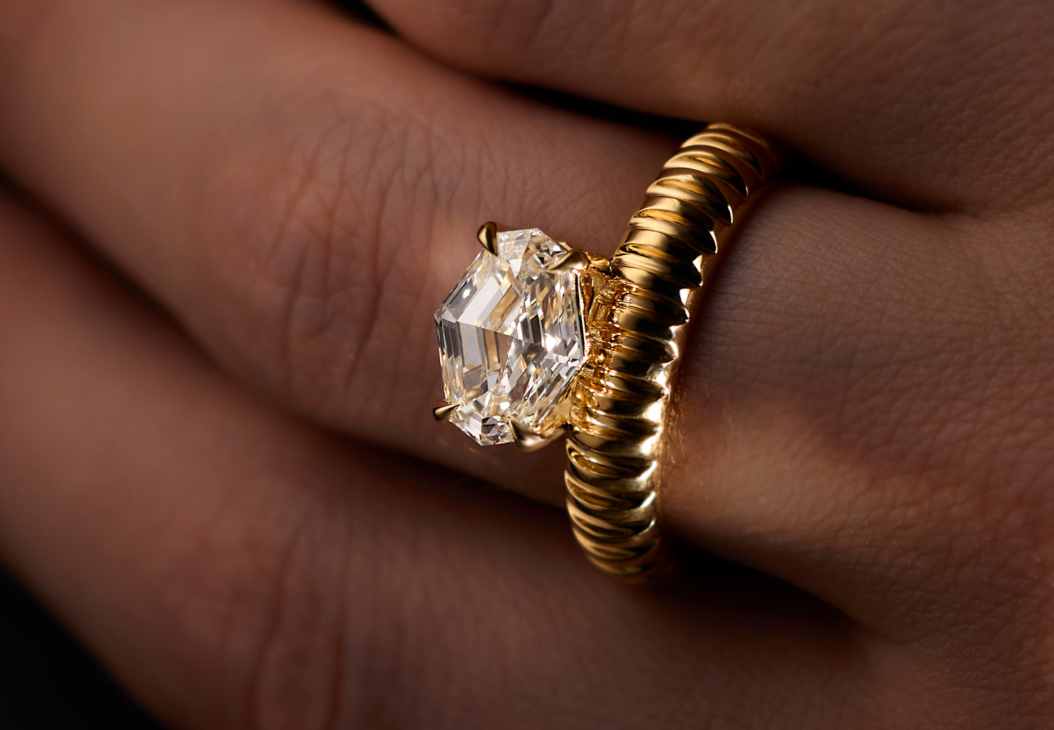 A close-up of a gold Leil architectural Auri ring with a fluted band and a large clear spike-cut diamond, worn on a finger.