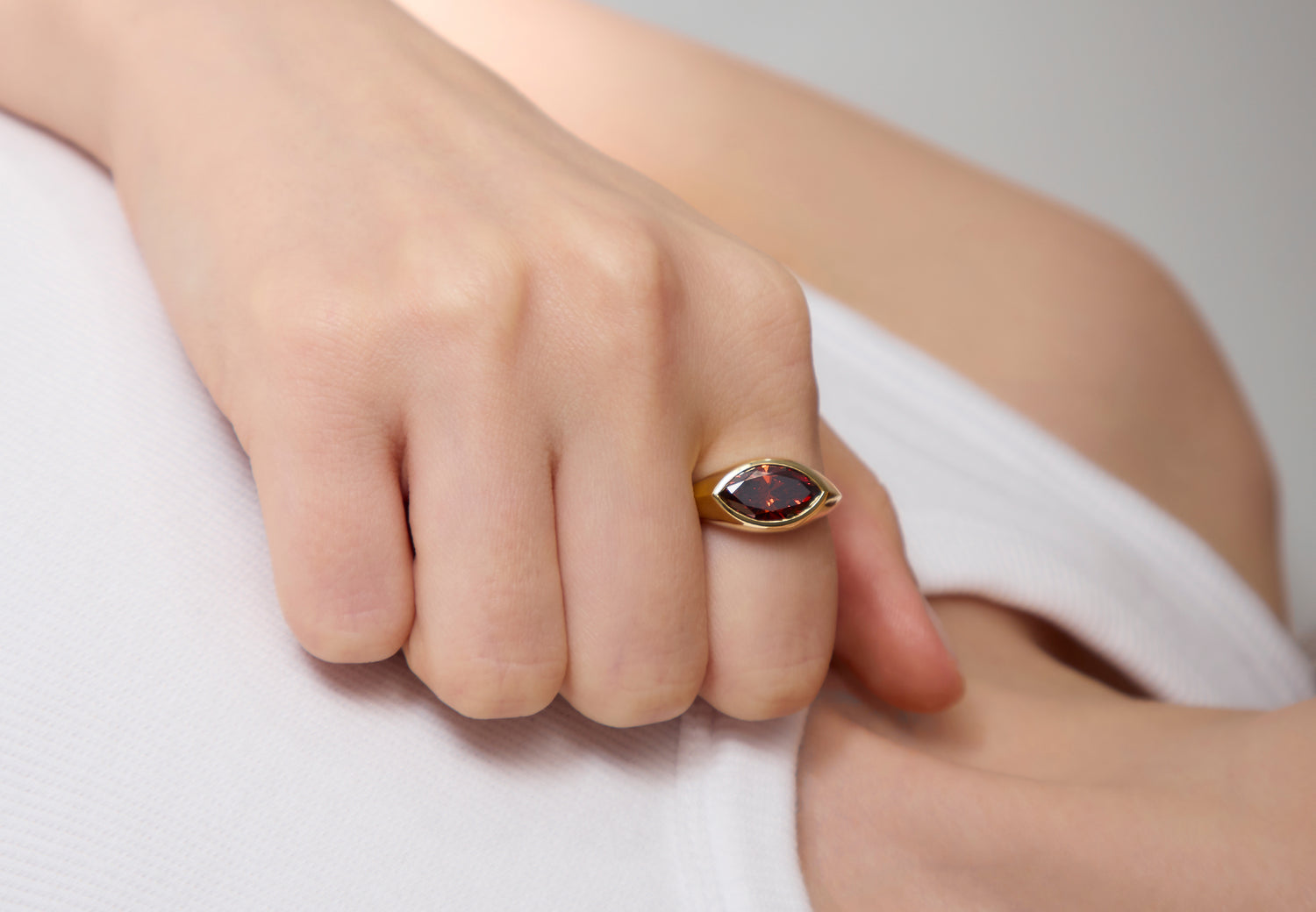 A close-up of a hand wearing a Leil yellow gold signature signet ring with a bezel-set, marquise-cut dark red diamond.