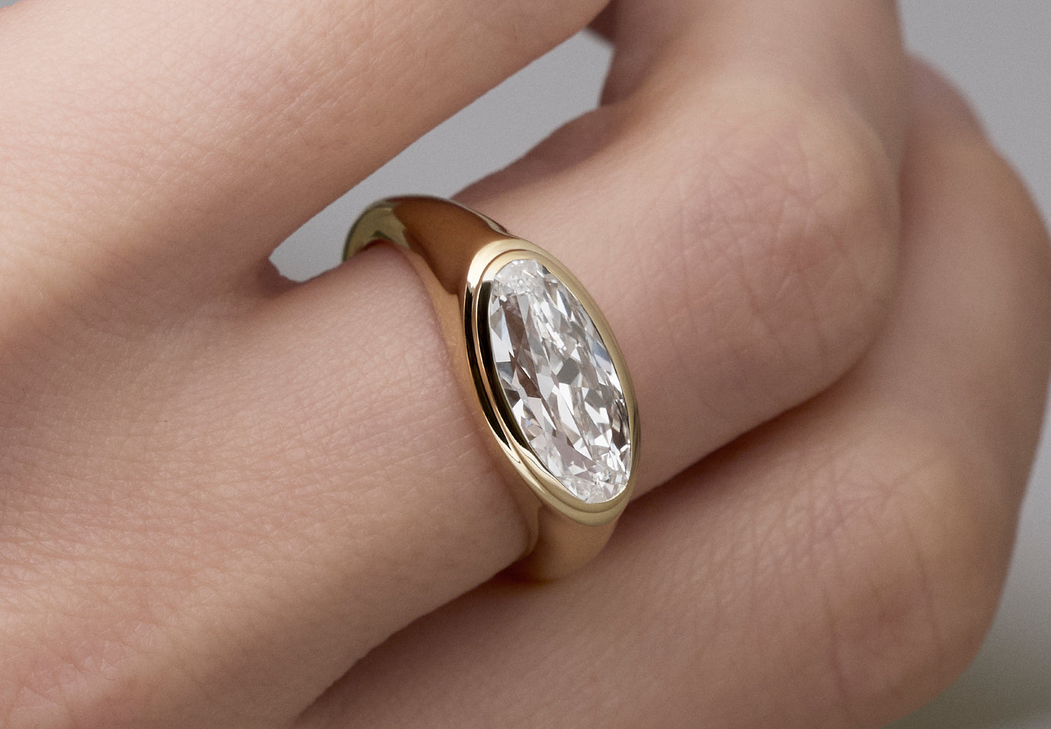 A close-up of a Leil yellow gold signet ring with a moval-cut, bezel-set lab grown diamond worn on a finger.