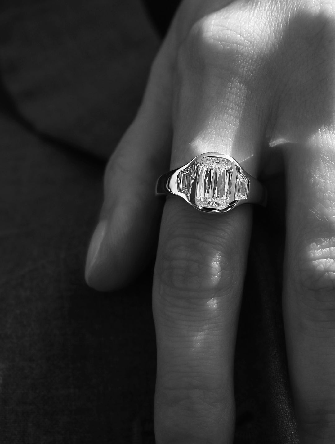 Close-up of a signature LEIL diamond signet ring on a finger with a black and white filter