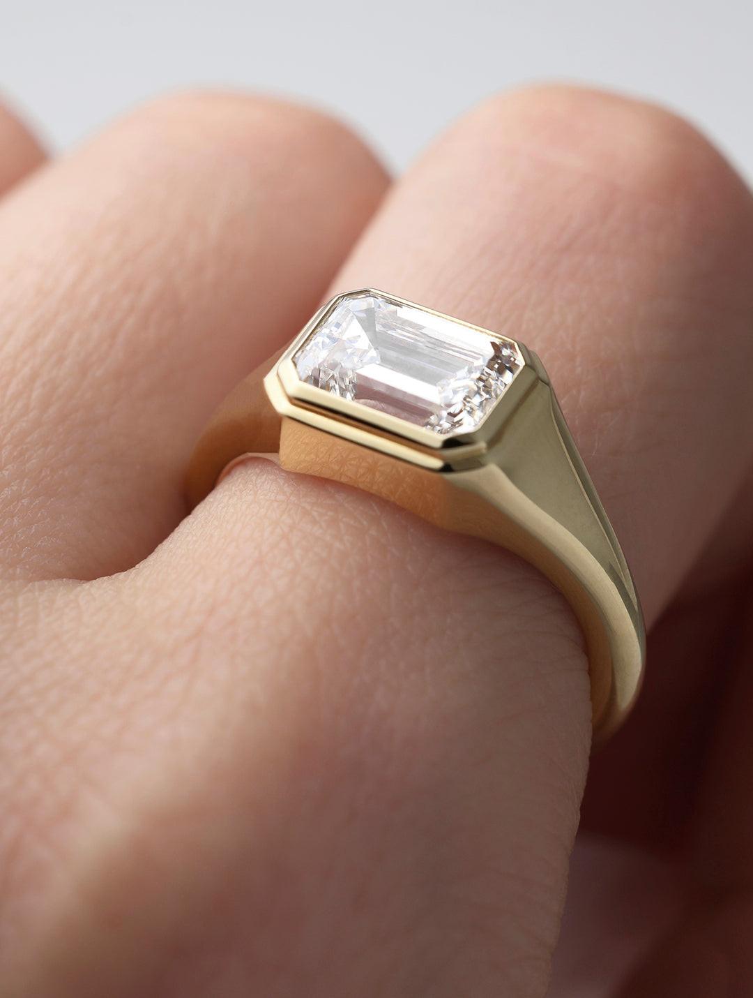 LEIL signature 18k solid gold Ahona bezel ring with a 2ct lab diamond on a finger against a neutral background