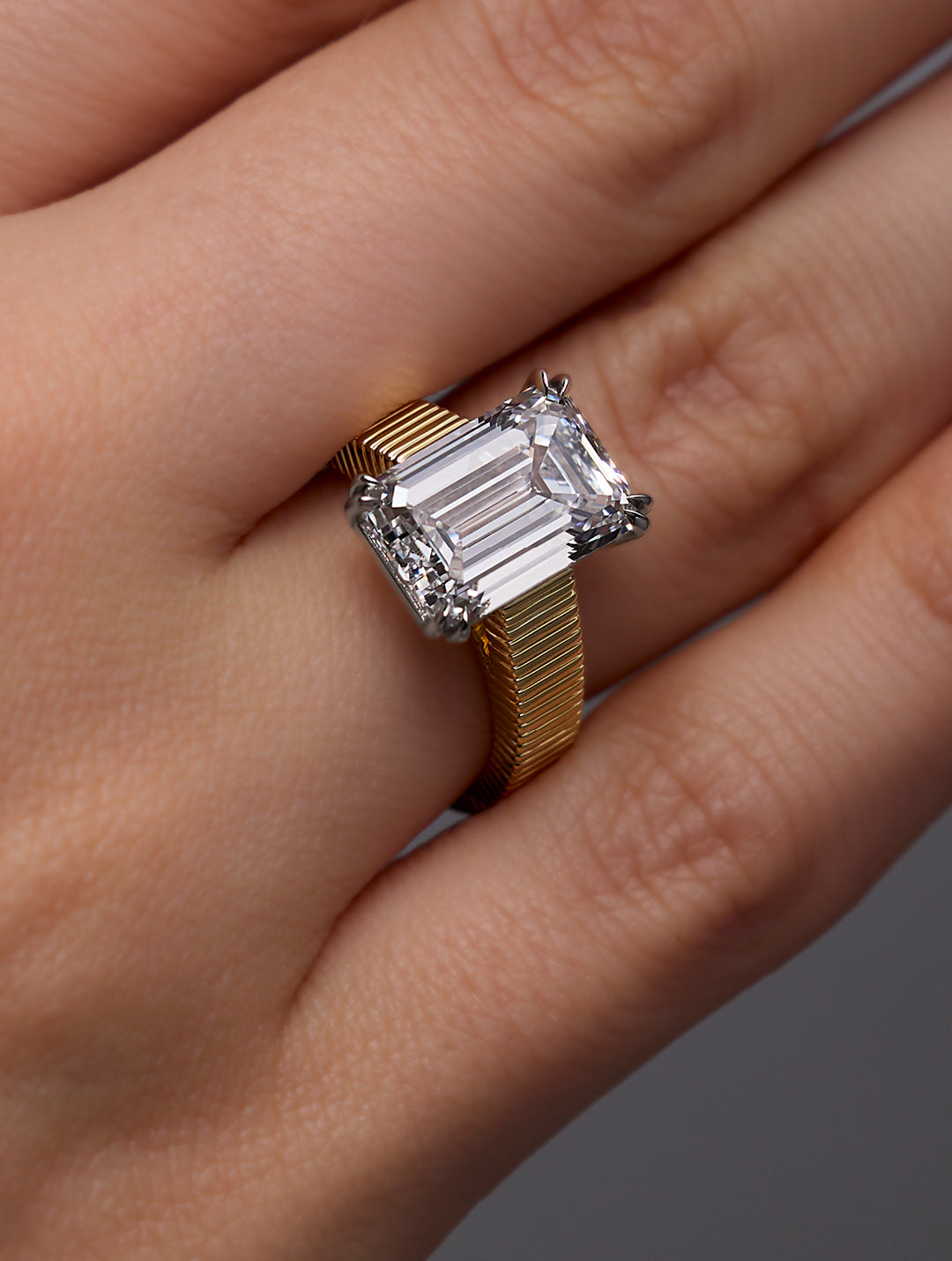 LEIL signature 18k solid gold Arra ring with a 5ct cathedral emerald-cut diamond on an architectural ribbed band on a dark background
