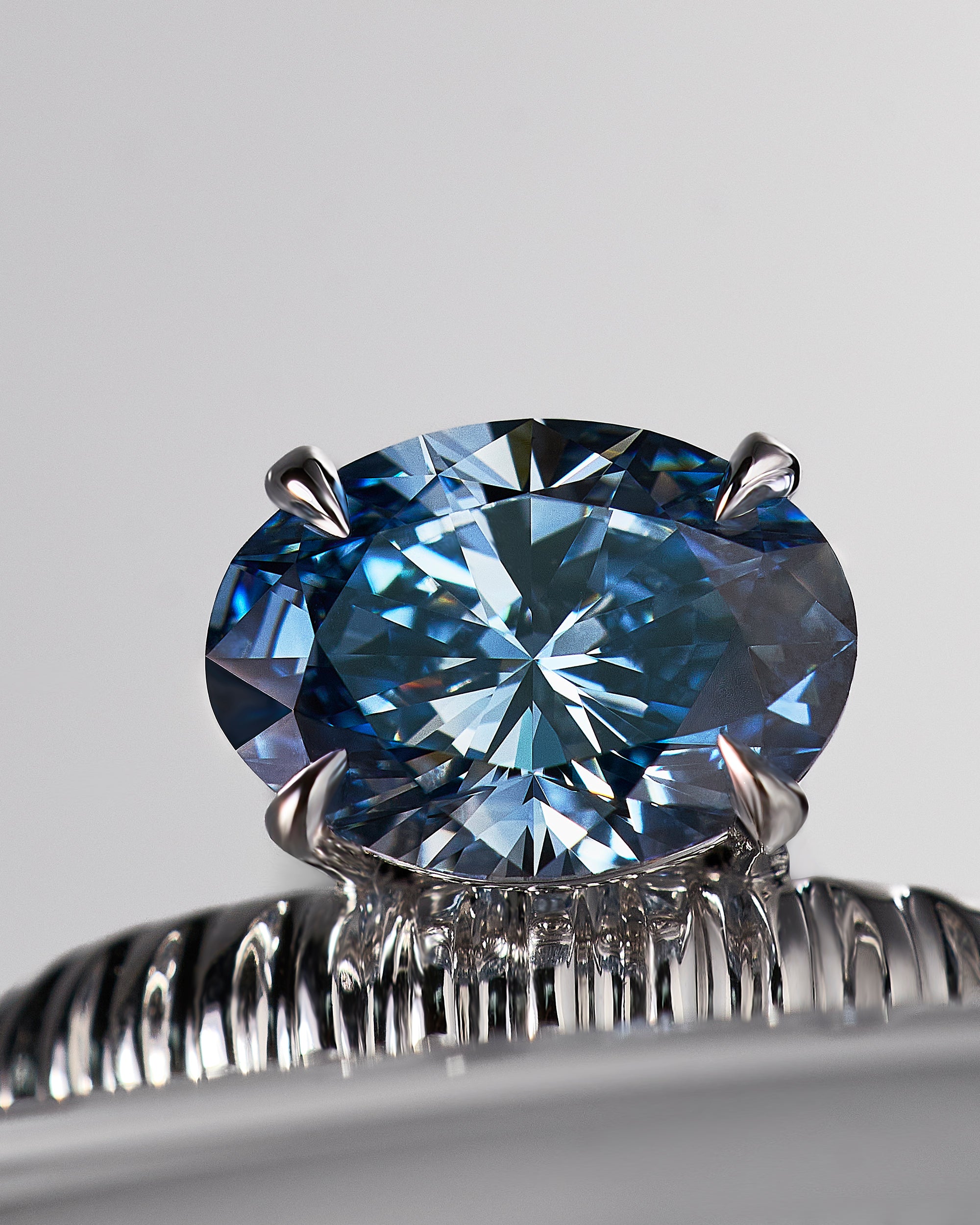 A close-up shot of a round brilliant-cut blue diamond ring, set in a white gold Leil signature architectural Auri band. The stone is shown in sharp focus against a clean, light gray background.