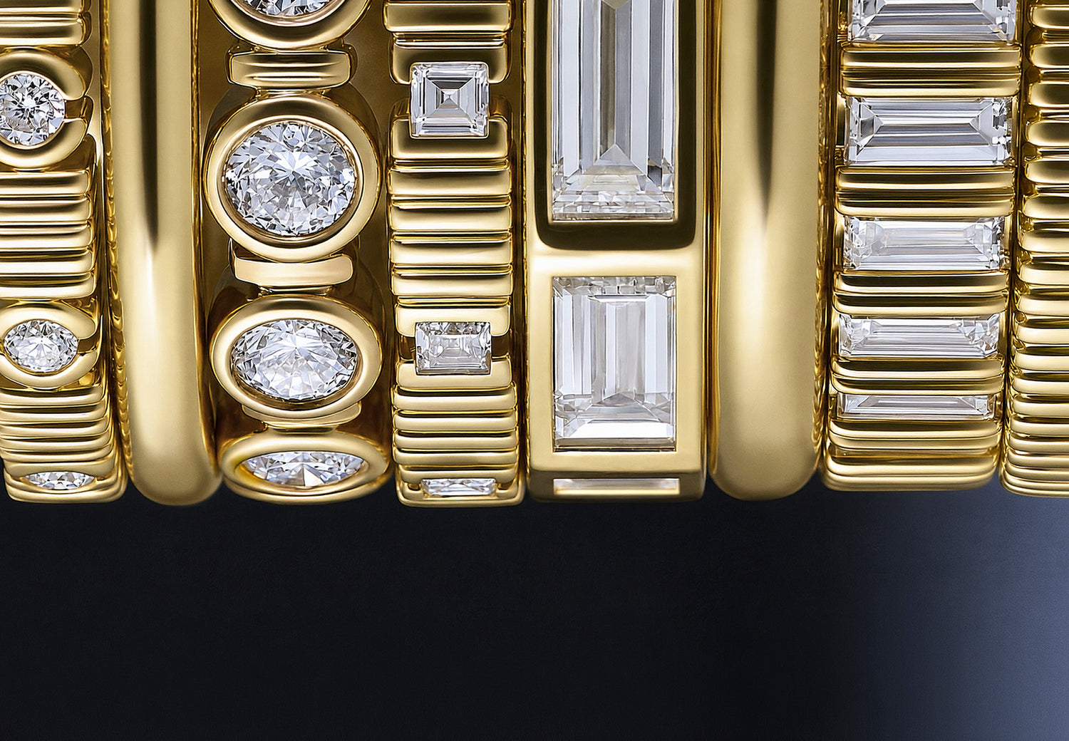 Close-up of a yellow gold stack of modular architectural rings featuring multiple diamond settings, including round, oval, and baguette cuts, set against a dark background.