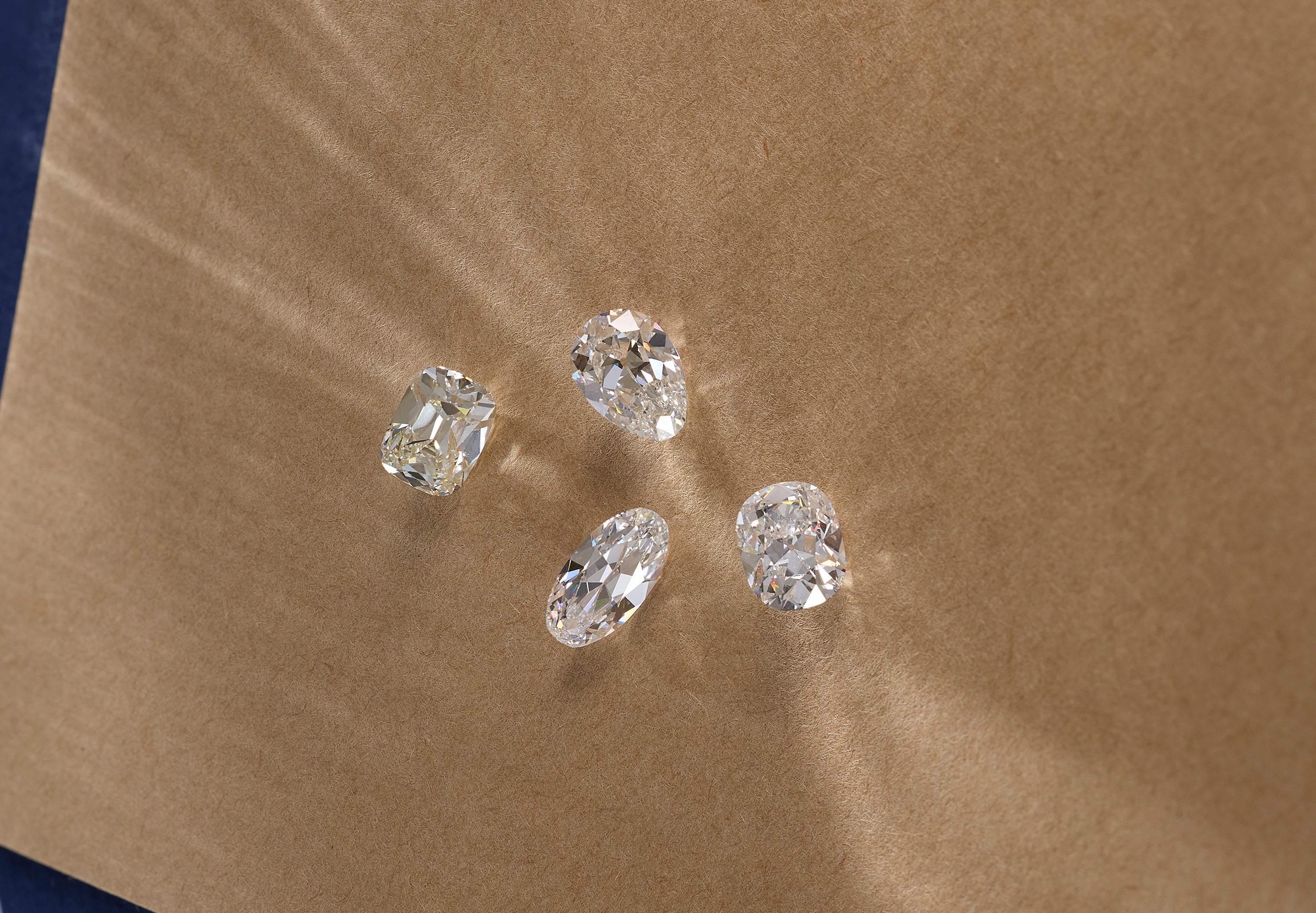 Four loose clear lab grown diamonds in different cuts arranged on a brown kraft paper background.