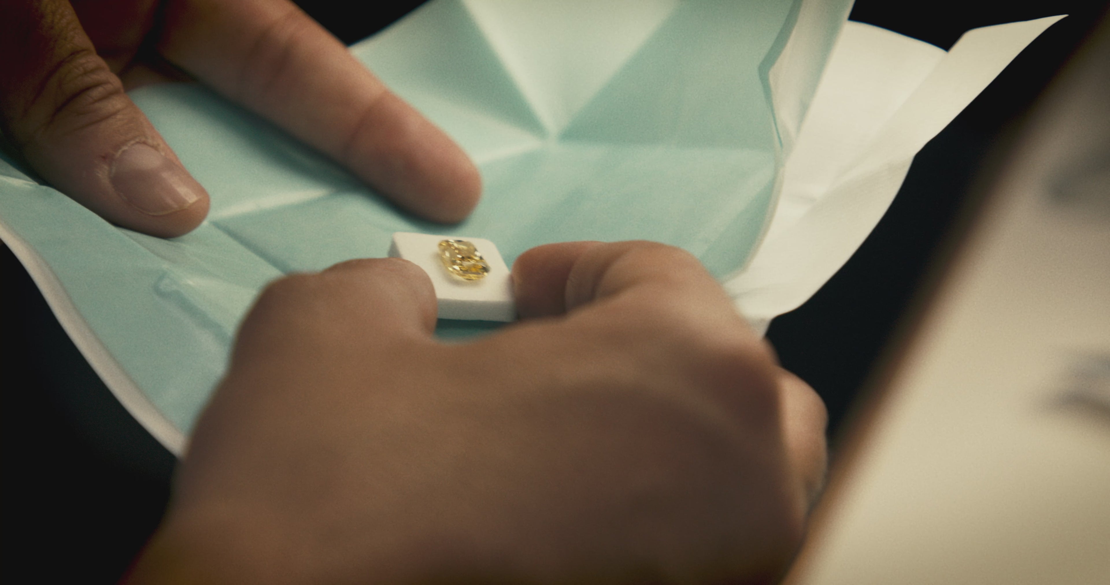 Load video: Close-up of a craftsman inspecting a finished lab-grown diamond in a custom yellow colour.
